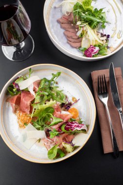 Yeşil salatalı lezzetli taze yemekler ve arka planda beyaz tabakta jambon dilimleri.