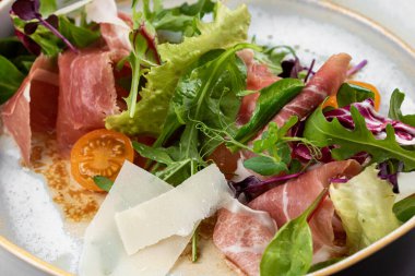 Taze salata ve arka planda beyaz tabakta peynirli jambon dilimleri.