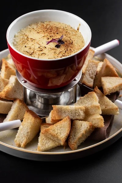 Classic swiss cheese fondue with white bread crackers on black table background