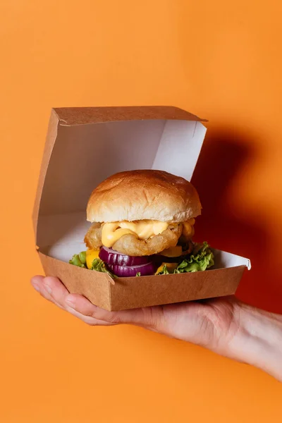 Elinde turuncu arka planda beyaz altın çöreklerle ızgara tavuk eti tutan kişi.