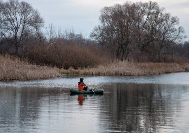 Spring landscape with a fisherman who fishes in an inflatable boat on the river