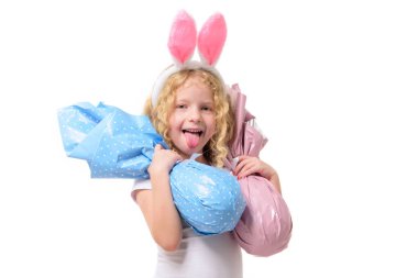 Paskalya tavşanı kulaklı şirin küçük kız iki doldurulmuş tavşana sarılıyor, izole edilmiş beyaz arka plan. Çocuk gülümsüyor. Boşluğu kopyala.