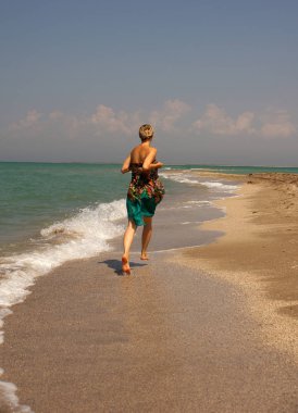 Genç kadın sahilde yalınayak koşuyor..