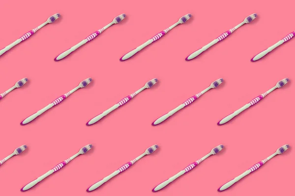 Много зубных щёток лежат на розовом фоне. — стоковое фото