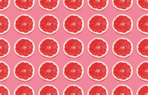Colorful fruit pattern of grapefruit slices on pink background.