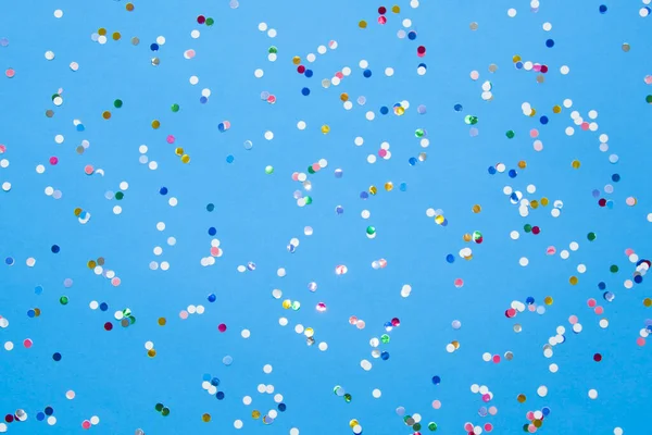 Colored confetti scattered on blue pastel paper lizenzfreie Stockbilder