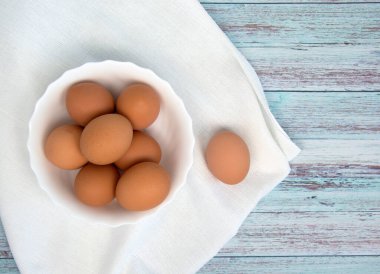 Tahta bir masanın üzerinde beyaz bir kasede duran doğal çiftlik yumurtaları. Çevre dostu ürün.