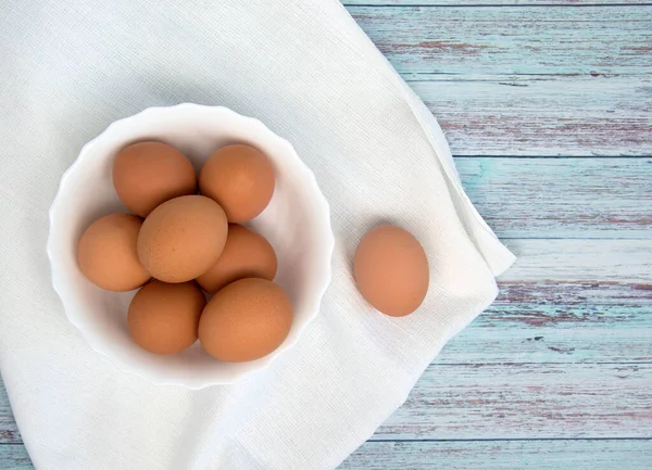 Természetes tanyasi tojás egy fehér tálban áll egy fa asztalon. Környezetbarát termék. Stock Kép