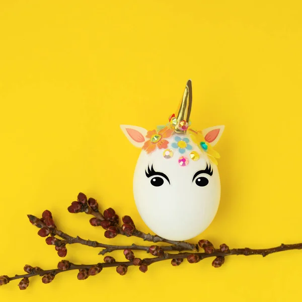 Paskalya konsepti. Tek boynuzlu at şeklinde yumurta. Ve tomurcuklu dallar ve çiçek açan yapraklar. Sarı arka planda..