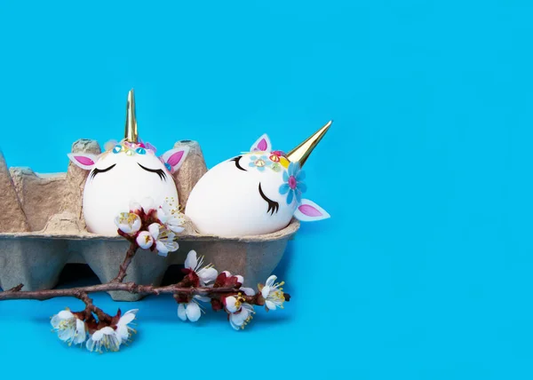 Paskalya konsepti. Yumurta şeklinde tek boynuzlu atlar. Mavi arka planda çiçek açan kiraz dalları