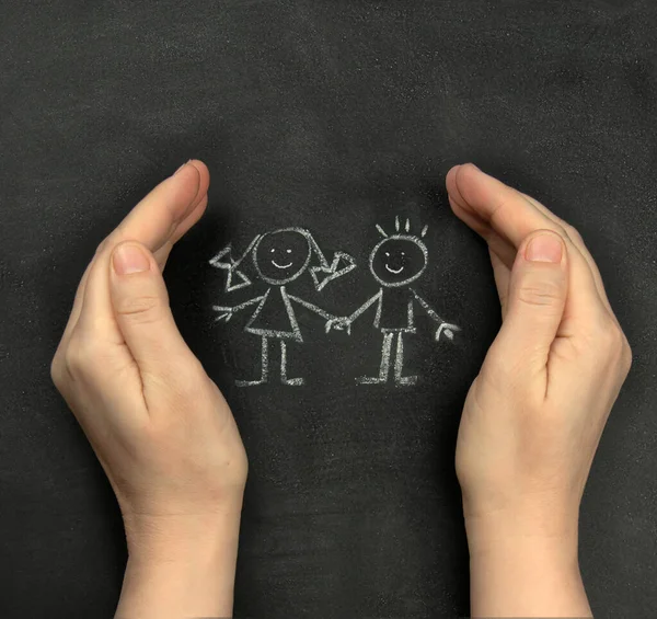 Hände schützen Kinder, die mit Kreide auf eine Tafel gezeichnet wurden. Konzept für den Internationalen Kindertag am 1. Juni Stockbild