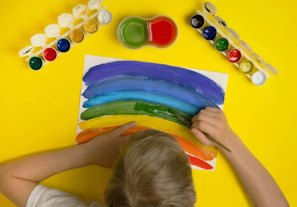 A child draws a rainbow with colors.