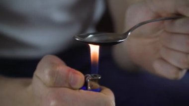 Bir uyuşturucu bağımlısı eroine hazırlanır. Kokain çakmağı kaşığı uyuşturucu sıvısıyla ısıtır.