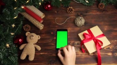 Ahşap arka plan üst görünüm siyah akıllı telefon ve yeşil ekran Noel süslemesi ile masada yatıyor 