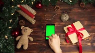 Ahşap arka plan üst görünüm siyah akıllı telefon ve yeşil ekran Noel süslemesi ile masada yatıyor 