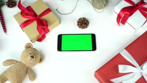 木製の背景トップビュークリスマスの休日の装飾とテーブルの上に横に緑の画面の黒いスマートフォン — ストック動画