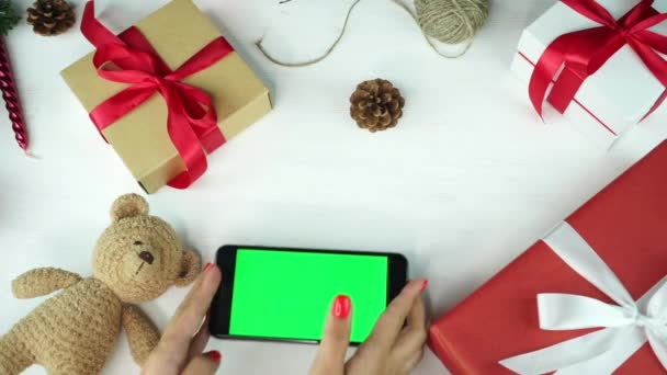 木製の背景トップビュークリスマスの休日の装飾とテーブルの上に横に緑の画面の黒いスマートフォン — ストック動画