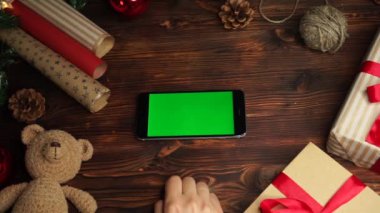 Ahşap arka plan üst görünüm siyah akıllı telefon ve yeşil ekran Noel süslemesi ile masada yatıyor 