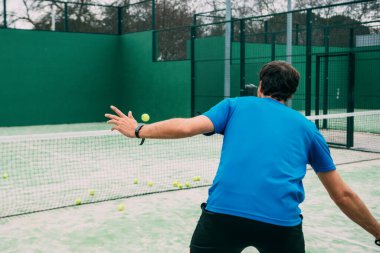 Yeşil kortta raket oynayan genç bir adam, mavi tişört giyiyor. Uzay konseptini kopyala.