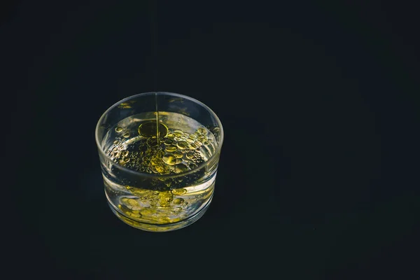 Huile d'olive tombant sur l'eau dans un verre bas avec des gouttes d'huile sur le dessus — Photo
