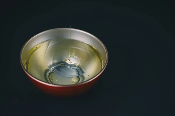 Azeite que cai na água e gota no vermelho e prata metálico bowl.Copy espaço — Fotografia de Stock