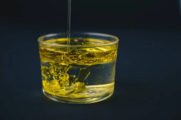 Olio d'oliva che cade sull'acqua in un bicchiere basso con gocce d'olio sul fondo . — Foto Stock