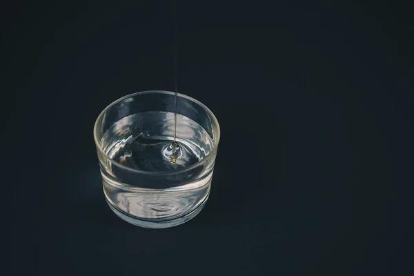 Azeite caindo na água em um copo baixo . — Fotografia de Stock