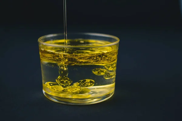Оливкова олія падає на воду в склянці з краплями олії на дні . — стокове фото