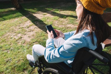 Tekerlekli sandalyede cep telefonunu kullanan engelli bir kız. Engelli ve teknoloji kavramı.