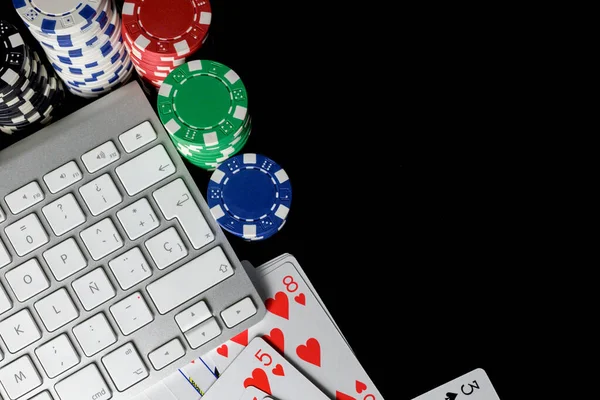 Cards and poker chips next to a computer keyboard isolated on a black background,gambling concept and online betting.Copy space