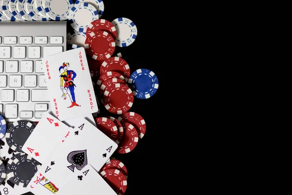Poker red,blue and white chips and cards surrounding a computer key board isolated on black background.Bet and online game concept.Copy space