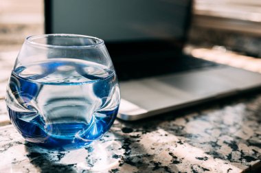 Sulu zarif mavi bardak. Arka planda odaklanmamış bir laptop var. Ofis kavramı