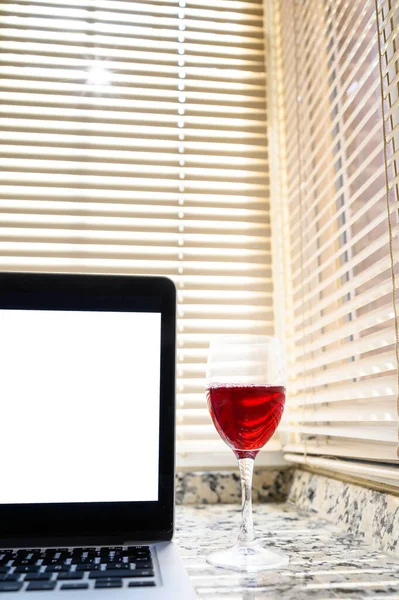 A glass of red wine and a laptop with a white screen. Vertical copy space.Relaxing time at home concept.
