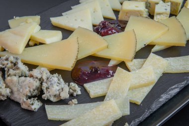 Küçük porsiyonlar halinde kesilmiş ve siyah bir arka planda siyah bir tabakta yemeye hazır lezzetli Avrupa peynirlerinin farklı türlerini kapatın. Kalite ve gurme yemek konsepti