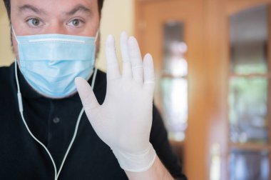 Korona virüsünden kurtulan ve hijyenik eldiven ve maske takan bir adam küresel sağlık karantinası sırasındaki video görüşmesi sırasında ailesine güven verici bir jest yaparak kamerayı selamlıyor. İyileşme, sağlık ve salgın hastalık kavramı