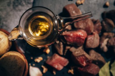 İçinde zeytinyağı, küçük et küpleri ve patates bulunan cam kase, arka planda siyah bir tahta üzerinde. Akdeniz diyetinin içeriği. Taze malzeme ve sağlıklı yiyecek kavramı