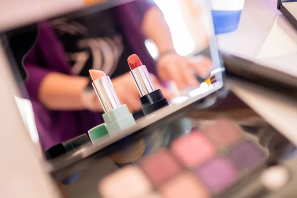 Lipsticks reflected in a make-up mirror where a woman is also reflected in an unfocused background. Feminine care and aesthetics