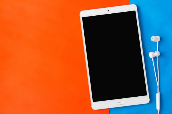 Tablet met oortelefoon op oranje / blauwe achtergrond — Stockfoto