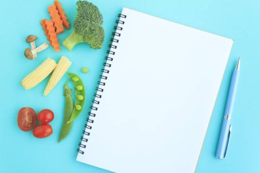 Sebzeler, defter ve kalem üst görünümde.