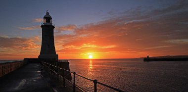 The sun rises between the piers at the mouth of the river Tyne at Tynemouth, England