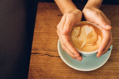 Kahve dükkanında bir fincan kahve tutan kadın elleri. Güzel köpük, seramik fincanlar, mesaj atmak için yer..