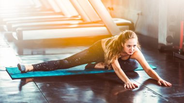 Spor salonundaki kadın esneme egzersizleri yapıyor ve zeminde gülümsüyor..