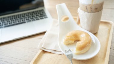 Laptop bilgisayarının önündeki masada kahve, çörek ve jöleli çöreklerle rahatlama..