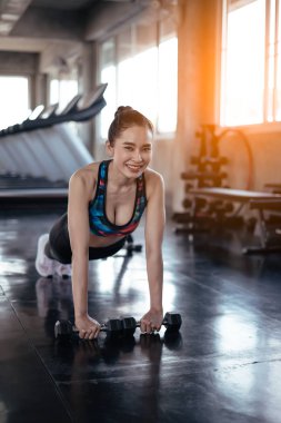 Slim woman doing push ups with heavy dumbbells while training in gym. 
