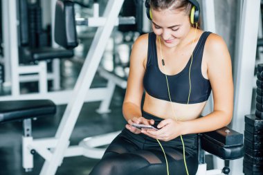 Spor salonunda akıllı telefon kullanan aktif bir kız. Genç kadın spor salonunda sağlıklı bir yaşam tarzında çalışıyor. Spor salonunda telefonu kullanan genç bir kadın. Sağlık konsepti değişikliği.