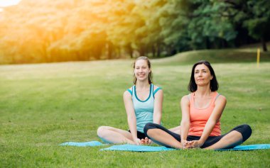 Yeşil çimenlerin üzerinde yoga yapan bir Yoga kadını. Dışarıda yoga dersine katılan bir grup yetişkin. Ailesi ya da arkadaşları yoga yapmayı seviyor..