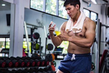 Asian man in gym holding electrolyte drink.