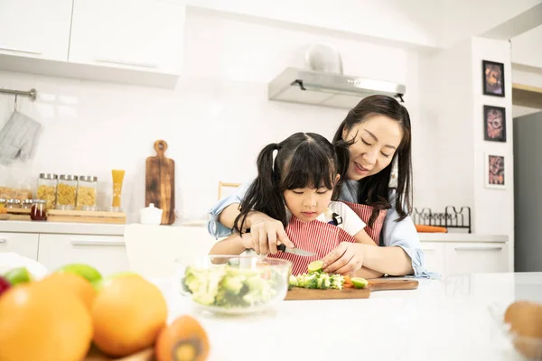 Young asian family cooking food in kitchen.Cute little girl and her beautiful parents are cutting vegetables and smiling while cooking in kitchen at home.Happy family in the kitchen concept.