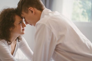 Young romantic cute couple sitting face to face together in bed.