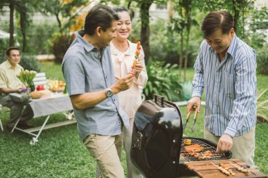 Aile ve arkadaşlar masada toplandı. Bir grup arkadaş için açık havada bbq pişiriyorlar. Büyük Aile Bahçesi Partisi Kutlaması. Komşuların İçki İçme Bahçesi Konsepti..